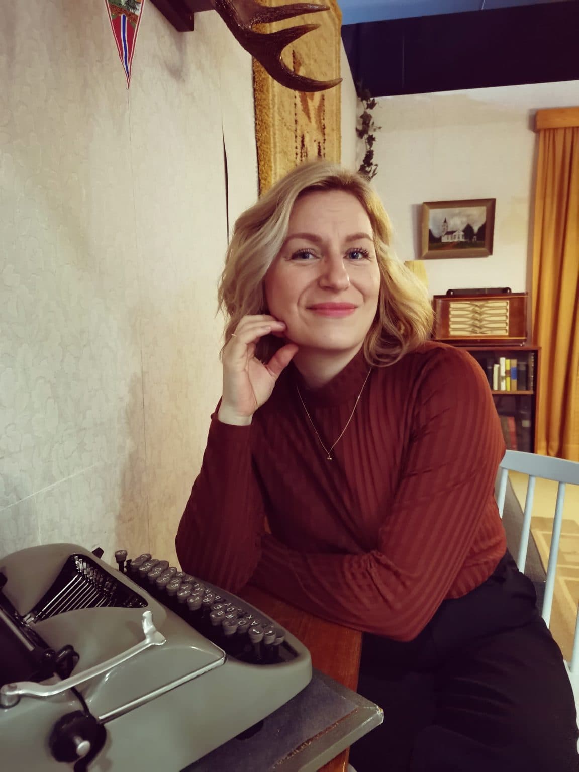 Marika Piira hymyilee vanhan kirjoituskoneen vieressä lämpimässä kotimiljöössä